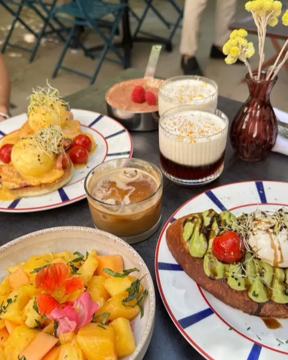 Brunch en terrasse: œufs bénédicte, tartine à l'avocat, assiette de fruits et cafés glacés.