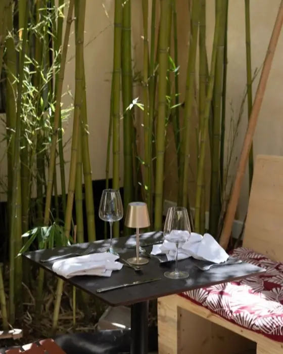 Table dressée près des bambous, verres à vin et serviettes pliées.
