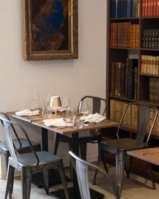 Salle et tables dressées devant les rayonnages, sous un tableau ancien.