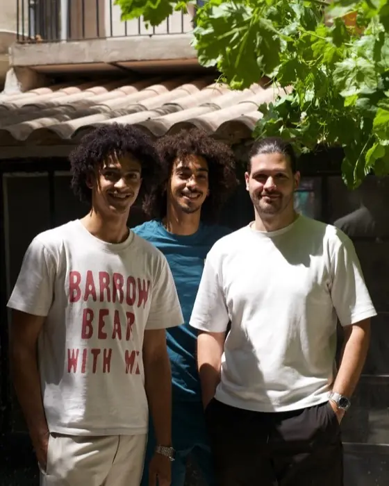 Trois personnes devant le lieu, sous la vigne.