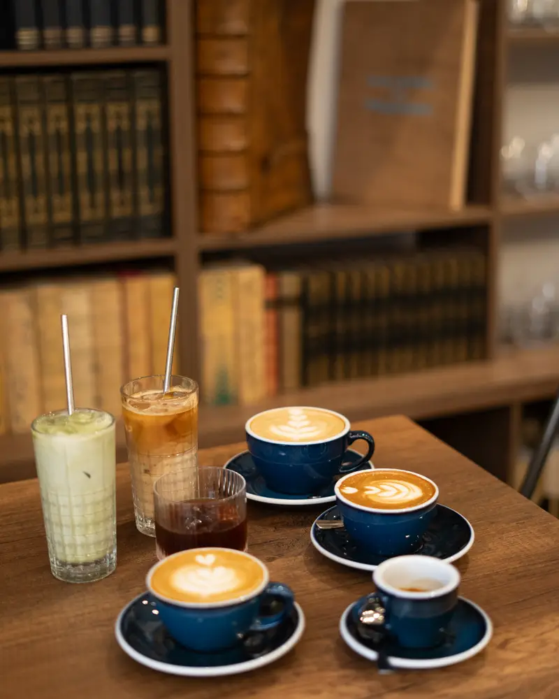 Tasses de café et boissons sur une table en bois, devant une bibliothèque.