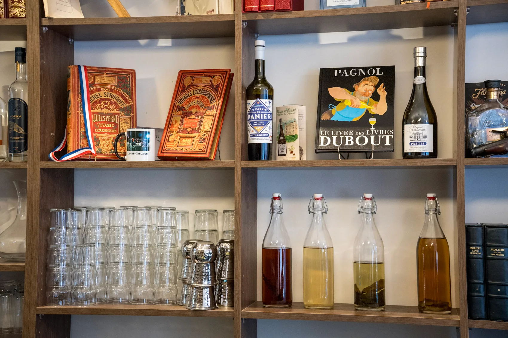 Étagères où se mêlent bouteilles, verrerie et livres anciens